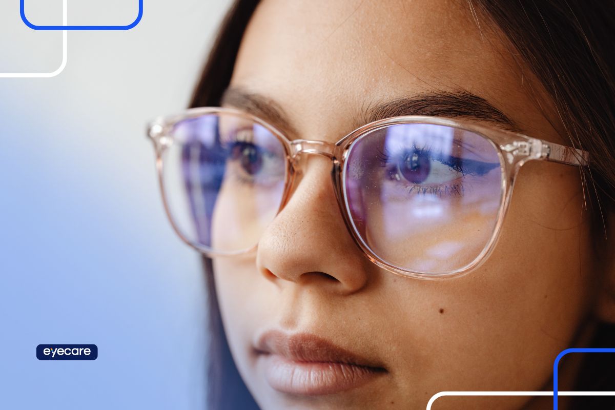 Close-up de uma mulher usando óculos com filtro de luz azul, destacando os olhos e refletindo a tela, simbolizando cuidados para prevenção de doenças oculares.